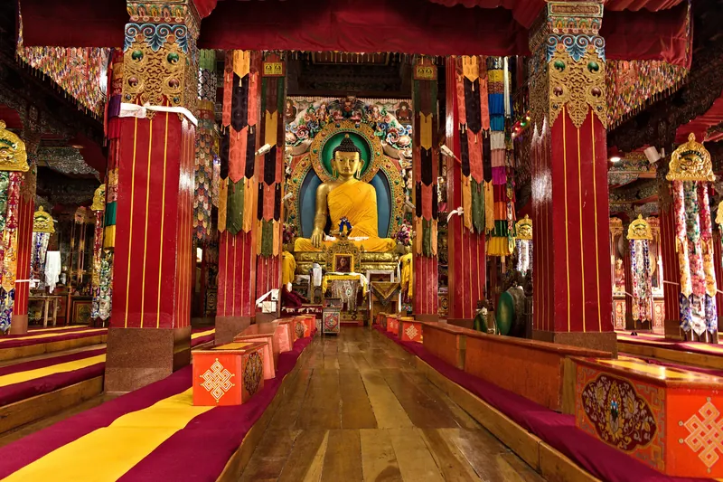 The prayer hall of Tawang Monastery — red columns, hanging silks and a gilded Buddha