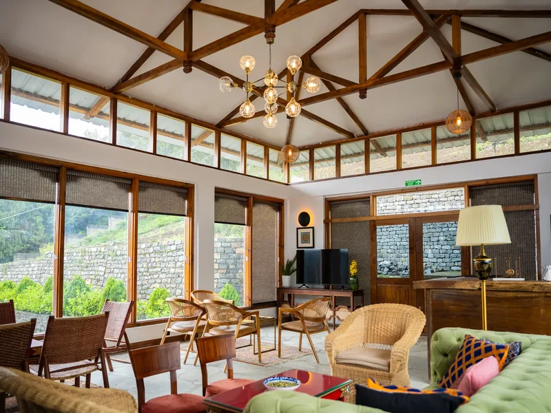 A lounge under a wood-truss ceiling, cane chairs facing the valley