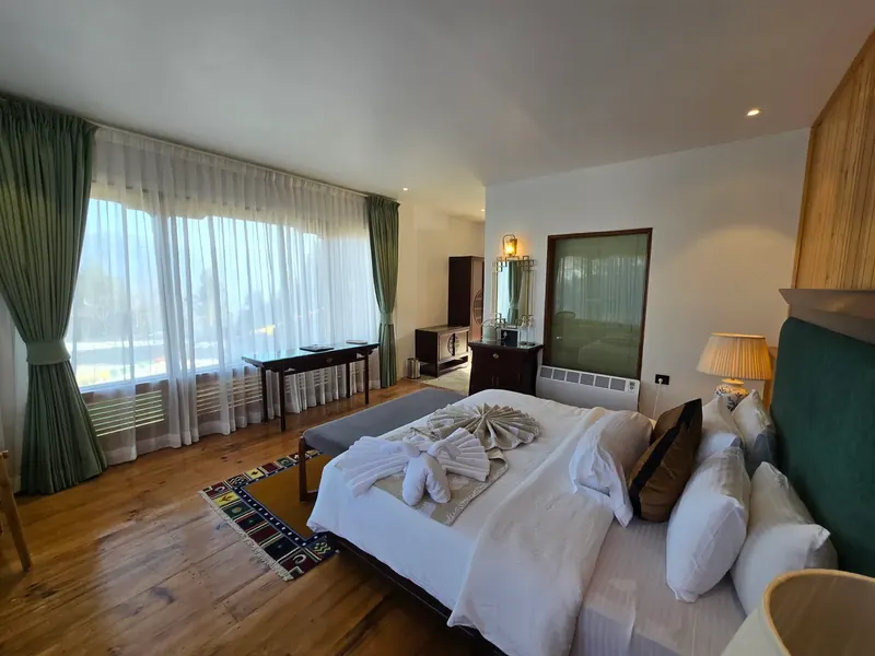 Green curtains drawn back onto the window wall, wardrobe and mirror beside the bed — Timilo Classic, Timilo Boutique